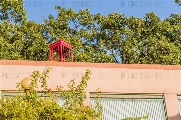 Red wooden telephone booth without glass on top of pink stucco building on sunny day with blue sky in South Korea