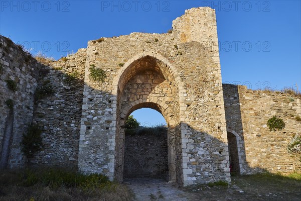 Old castle gate in a stone ruin surrounded by grass and clear blue sky above, sea fortress Methoni, Peloponnese, Greece, Europe