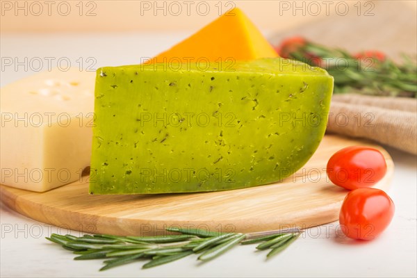 Green basil cheese and various types of cheese with rosemary and tomatoes on wooden board on a white wooden background. Side view, close up, selective focus