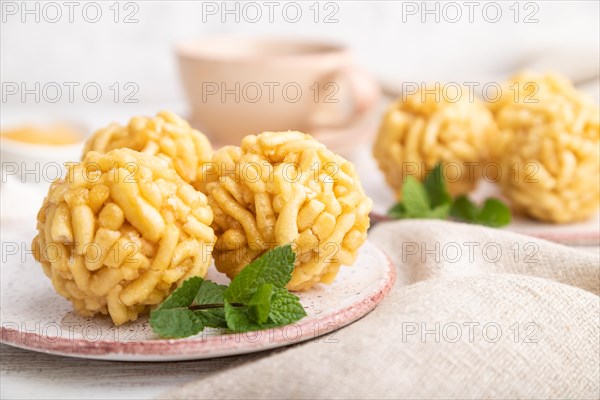 Traditional Tatar candy chak-chak made of dough and honey with cup of coffee on a white wooden background and linen textile. Side view, close up, selective focus