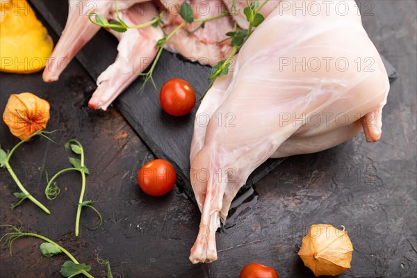 Whole raw rabbit with pumpkin, tomatoes, pea sprouts on a black concrete background and linen textile. Side view, close up, selective focus