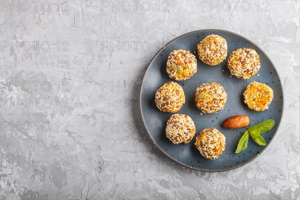 Energy ball cakes with dried apricots, sesame, linen, walnuts and dates with green mint leaves on a blue ceramic plate on a gray concrete background. top view, copy space, flat lay. vegan homemade candy