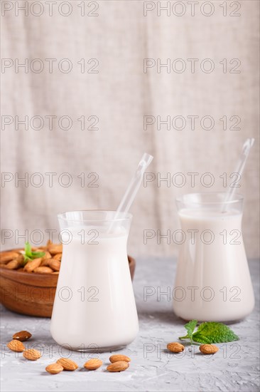 Organic non dairy almond milk in glass and wooden plate with almond nuts on a gray concrete background. Vegan healthy food concept, close up, side view, copy space