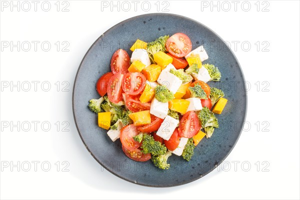 Vegetarian salad with broccoli, tomatoes, feta cheese, and pumpkin on a blue ceramic plate isolated on white background, top view, close up