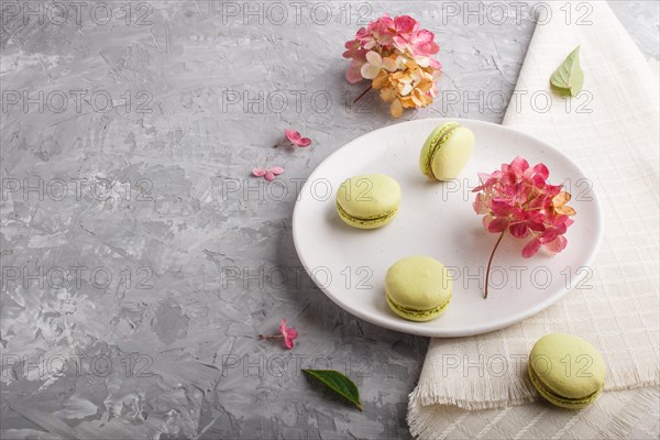 Green macarons or macaroons cakes on white ceramic plate on a gray concrete background and linen textile. side view, copy space