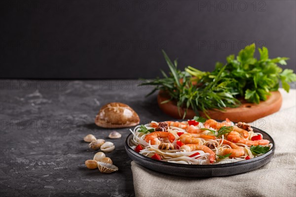 Rice noodles with shrimps or prawns and small octopuses on gray ceramic plate on a black concrete background and linen textile. side view, copy space, selective focus