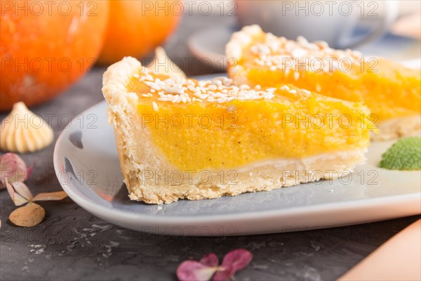 Two pieces of traditional american pumpkin pie with cup of coffee on a black concrete background and orange textile. side view, close up, contrast, selective focus