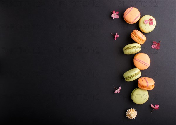 Orange and green macarons or macaroons cakes on black background. top view, flat lay, copy space