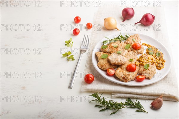 Fried pork chops with tomatoes and herbs on a white ceramic plate on a white wooden background and linen textile. side view, copy space