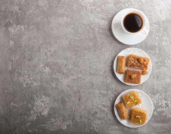 Traditional arabic sweets (basbus, kunafa, baklava) on white plate and a cup of coffee on a gray concrete background. top view, flat lay, copy space