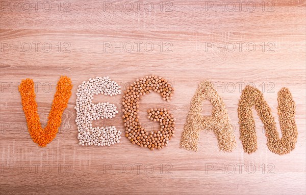 Word Vegan made of lentils, buckwheat, beans, rice and chickpeas on a wooden background