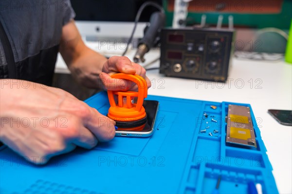 Close-up of a man using suction cup to press the screen of a mobile to attach it in a workshop