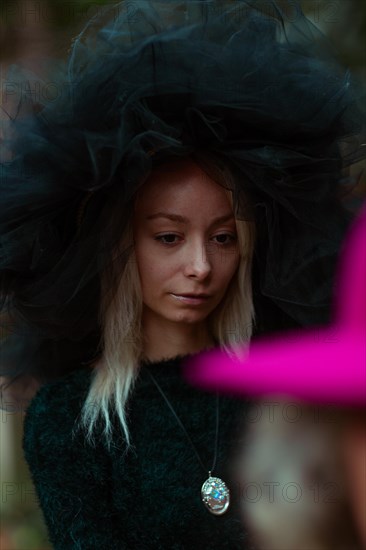 Woman in a tulle hat, the selective focus brings attention to her face and colorful necklace