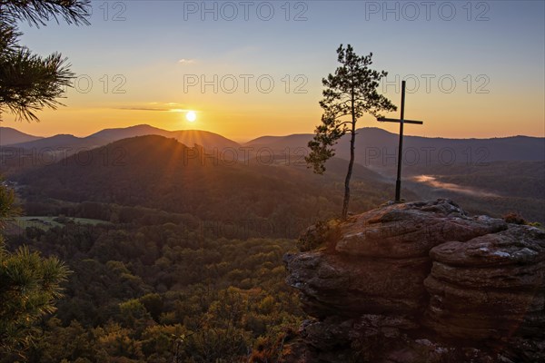Sunrise on the Roetzenfelsen in the Palatinate Forest with bright sunshine and the lone pine tree and the summit cross on the red rock