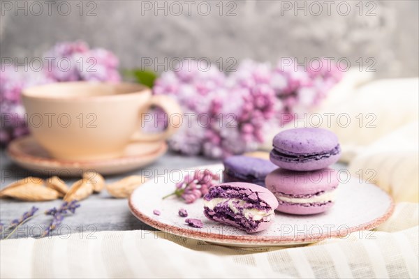 Purple macarons or macaroons cakes with cup of coffee on a gray wooden background and white linen textile. Side view, close up, selective focus