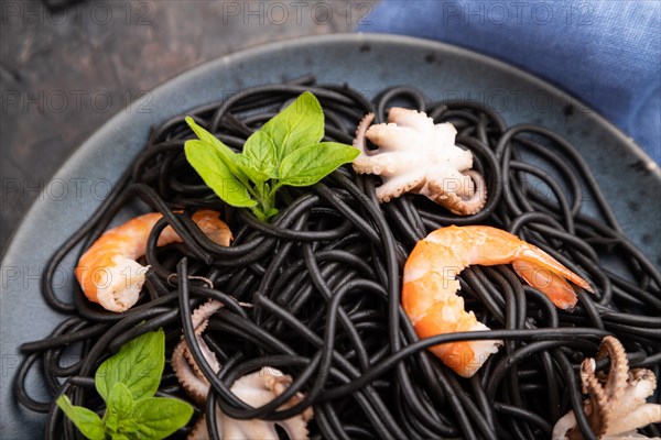 Black cuttlefish ink pasta with shrimps or prawns and small octopuses on black concrete background and blue textile. Top view, close up, selective focus