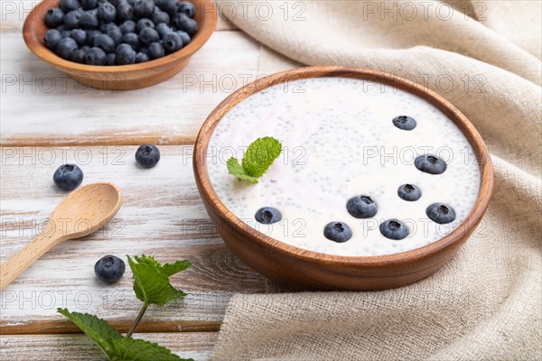 Yogurt with blueberry in wooden bowl on white wooden background and linen textile. Side view, close up