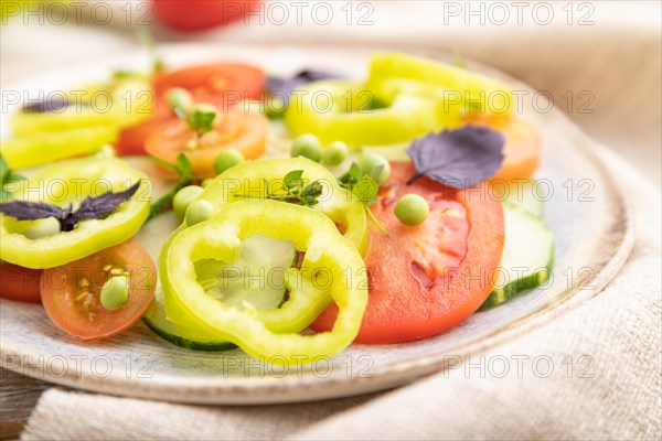 Vegetarian salad from green pea, tomatoes, pepper and basil on white wooden background and linen textile. Side view, close up, selective focus