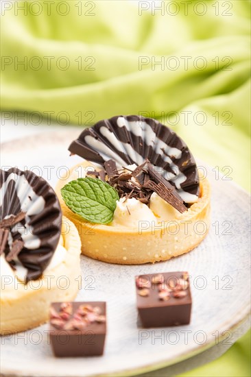 Sweet tartlets with chocolate and cheese cream with cup of coffee on a gray concrete background and green textile. Side view, close up, selective focus