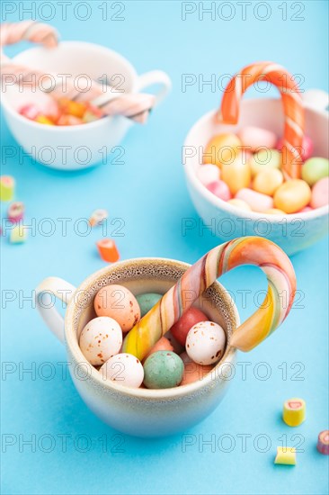 Heap of multicolored caramel candies in cups on blue pastel background. close up, side view, selective focus