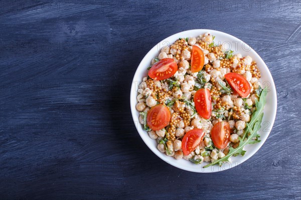 Vegetarian salad of boiled chickpeas, cheese, arugula, mustard and cherry tomatoes on black wooden background. copy space, top view