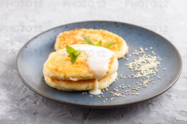 Cheese pancakes on a blue ceramic plate with milk sauce on a gray concrete background. side view, close up, selective focus