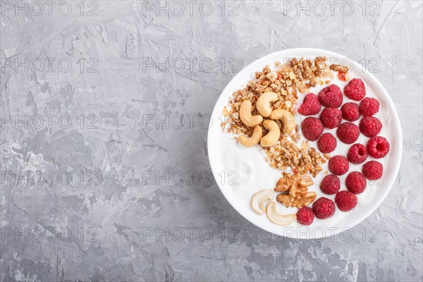 Yoghurt with raspberry, granola, cashew and walnut in white plate on gray concrete background and linen textile. top view, flat lay, copy space