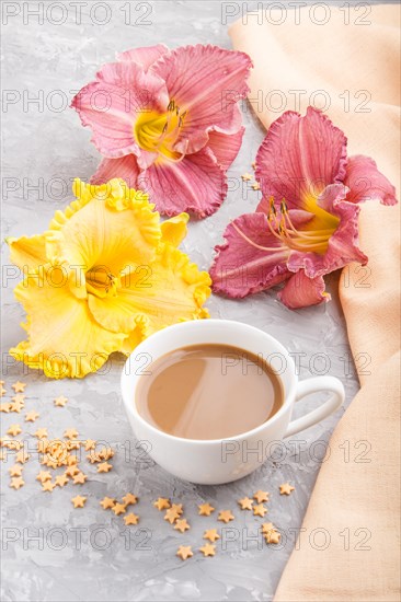 Yellow anf purple day-lilies cup of coffee on a gray concrete background, with orange textile. Morninig, spring, fashion composition, side view, close up