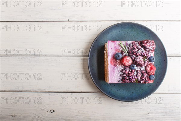 Berry cake with milk cream and blueberry jam on blue ceramic plate on a white wooden background. top view, flat lay, copy space