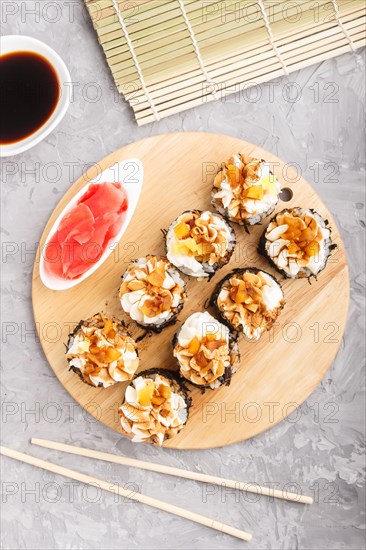 Japanese maki sushi rolls with cream cheese, chopsticks, soy sauce and marinated ginger on wooden board on a gray concrete background. Top view, flat lay, close up