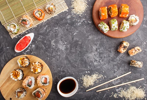 Different kinds of Japanese maki sushi rolls with salmon, sesame, cheese, roe and chopsticks, soy sauce, marinated ginger on a black concrete background. Top view, flat lay, copy space