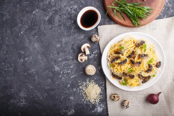 Rice noodles with champignons mushrooms, egg sauce and oregano on white ceramic plate on a black concrete background. Top view, flat lay, copy space