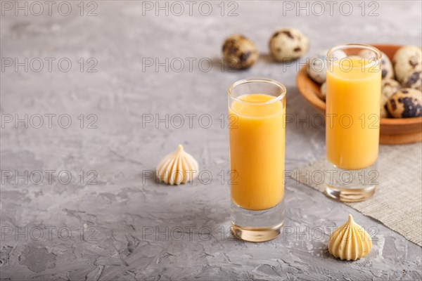 Sweet egg liqueur in glass with quail eggs and meringues on a gray concrete background. Side view, copy space