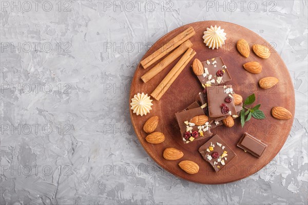 A pieces of milk chocolate with almonds and dried fruits on a brown wooden board on a gray concrete background. top view, copy space, flat lay