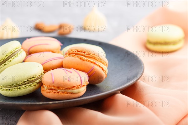 Orange and green macarons or macaroons cakes on blue ceramic plate on a gray concrete background. side view, close up, selective focus