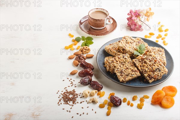Homemade granola from oat flakes, dates, dried apricots, raisins, nuts in blue ceramic plate with a cup of coffee on a white wooden background. Side view, copy space