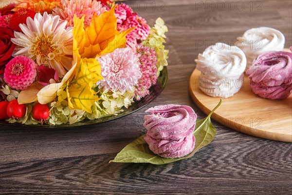 Pink and white marshmallows (zephyr) on a round wooden board with floral composition on a gray wooden background