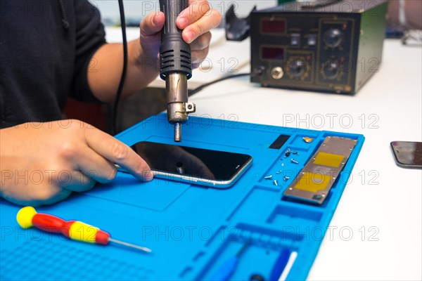 Close-up of a unrecognizable male technician fixing a mobile phone using a soldering iron in a workshop