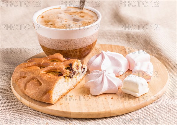 Sweet buns, meringues and coffee cup on a wooden board and linen tablecloth