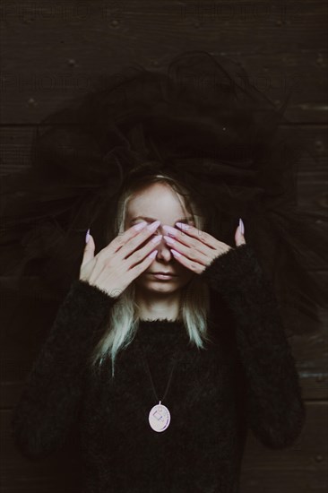 A woman in a black outfit with a large hat covers her eyes, creating a sense of drama