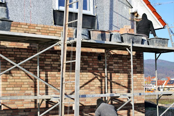 Bricklaying, clinker brick work. Bricklayers clad the facade of a detached house with clinker bricks