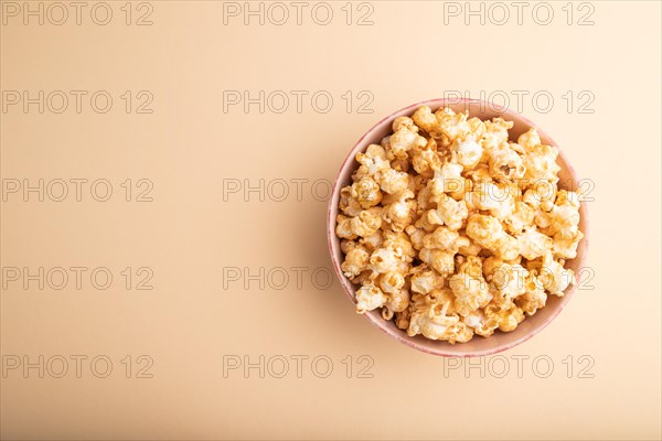 Popcorn with caramel in ceramic bowl on pastel orange background. Top view, flat lay, copy space