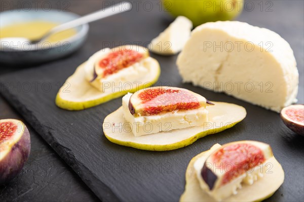 Summer appetizer with pear, cottage cheese, figs and honey on slate board on a black concrete background. Side view, close up, selective focus