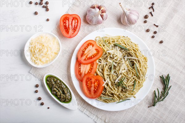 Spaghetti pasta with pesto sauce, tomatoes and cheese on a linen tablecloth on white wooden background. top view, flat lay