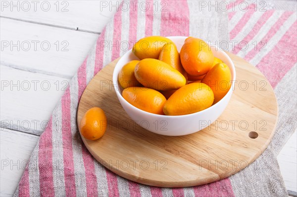 Kumquats in a white plate on a white wooden background, close up