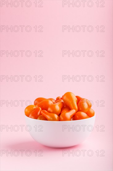 Fresh orange grape tomatoes in white ceramic bowl on pink pastel background. side view, close up, copy space
