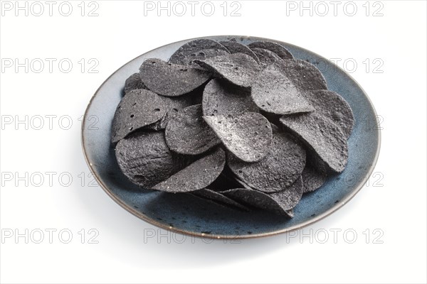 Black potato chips with charcoal on a blue ceramic plate isolated on white background. side view, close up