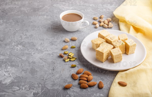 Traditional indian candy soan papdi in white plate with almond, pistache and a cup of coffee on a gray concrete background with yellow textile. side view, copy space