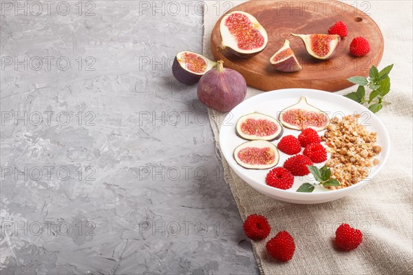 Yoghurt with raspberry, granola and figs in white plate on a gray concrete background and linen textile. side view, copy space