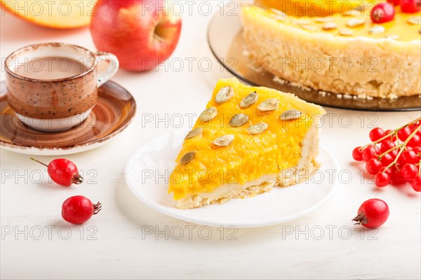 Traditional american sweet pumpkin pie decorated with hawthorn red berries and pumpkin seeds with cup of coffee on a white wooden background. side view, close up, selective focus